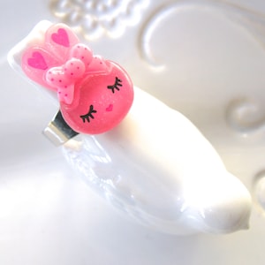 K&ouml;nnte beinhalten: Ein rosa Haarspange mit einem Hasenmotiv, Schleife und Herzakzenten. Die Spange zeigt ein Cartoon-Hasengesicht mit geschlossenen Augen und Wimpern. Das Haaraccessoire besteht aus gl&auml;nzendem Material und hat einen silbernen Metallclip.
