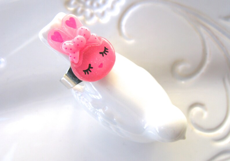 K&ouml;nnte beinhalten: Ein rosa Haarspange mit einem Hasenmotiv, Schleife und Herzakzenten. Die Spange zeigt ein Cartoon-Hasengesicht mit geschlossenen Augen und Wimpern. Das Haaraccessoire besteht aus gl&auml;nzendem Material und hat einen silbernen Metallclip.