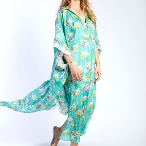May include: A woman wearing a long, flowing green and white floral print kaftan with a white trim. She is wearing white sandals and has long blonde hair.