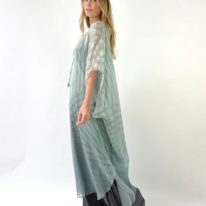 May include: A flowing, floor-length dress in shades of blue and gray. The outer layer features a sheer, patterned overlay, while the underlayer is a solid, darker gray. The dress has wide sleeves and a loose, comfortable fit, suitable for casual wear.
