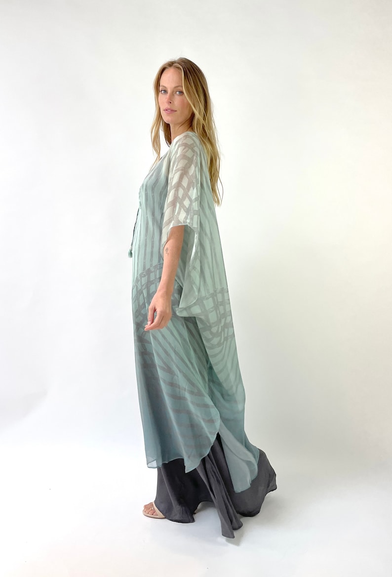 May include: A flowing, floor-length dress in shades of blue and gray. The outer layer features a sheer, patterned overlay, while the underlayer is a solid, darker gray. The dress has wide sleeves and a loose, comfortable fit, suitable for casual wear.