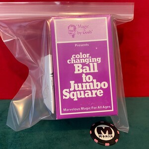 May include: A purple box with the text "color changing Ball to Jumbo Square" is inside a clear plastic bag. The box also has the text "Magic by Gosh" and "Marvelous Magic For All Ages". A black and pink magic chip is also visible.