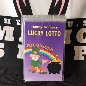 May include: A purple booklet with the title "Danny Archer's Lucky Lotto Pot O' Gold" featuring a cartoon leprechaun holding a pot of gold.