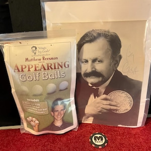 May include: A clear plastic bag of "Appearing Golf Balls" with text and images, next to a signed black and white photo of a man holding a coin. A poker chip with the letter "M" is also visible.