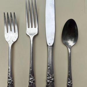 May include: A set of four silver-plated flatware pieces, including a knife, fork, and spoon. The handles are decorated with a floral design.