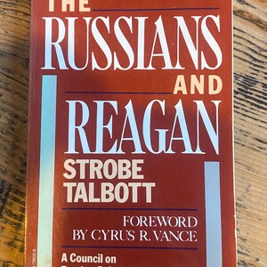 Può includere: Una copertina di libro vintage con sfondo rosso e testo bianco. Il titolo è "The Russians and Reagan" di Strobe Talbott. Il libro è un libro del Council on Foreign Relations con una prefazione di Cyrus R. Vance.