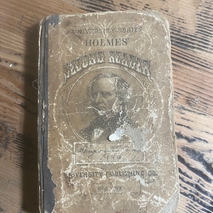 Puede incluir: Un libro antiguo titulado "Holmes' Second Reader" con una portada marrón descolorida y un retrato en blanco y negro de un hombre en la parte delantera. El libro forma parte de la "University Series" y fue publicado por "University Publishing Co. New York."