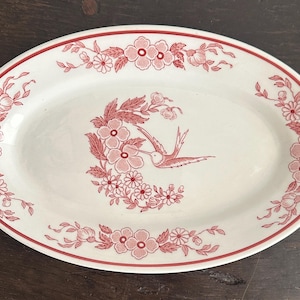 May include: A white oval serving dish with a red floral design and a hummingbird in the center.