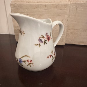 May include: White ceramic creamer with a floral design in shades of pink, blue, and green.