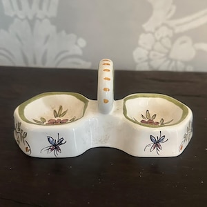 Può includere: Set di saliera e pepe in ceramica bianca con manico. Le saliere hanno un bordo verde e disegni floreali con accenti arancioni, rossi e verdi. Il manico ha punti arancioni.