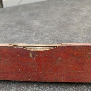 May include: A vintage wooden level with a brass level indicator. The level is red and has a worn finish.