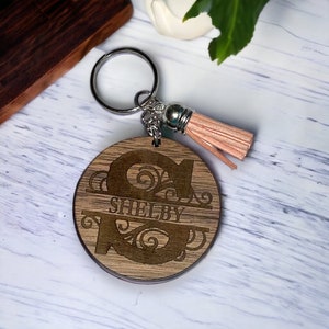 May include: A wooden keychain with a large letter "S" and the name "Shelby" engraved on it. The keychain has a silver key ring and a pink tassel.