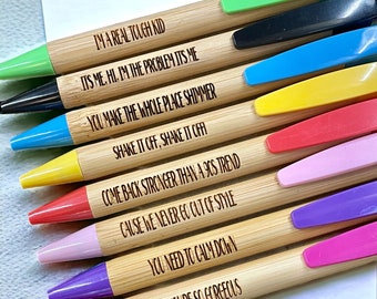 May include: A collection of bamboo pens with colorful tops. Each pen has a different color top and a unique engraved phrase, including "I'M A REAL TOUGH KID" and "YOU'RE SO GORGEOUS". The pens are arranged diagonally.