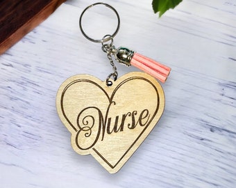 May include: A wooden heart-shaped keychain with the word "Nurse" engraved on it. The keychain has a silver ring and a pink tassel.