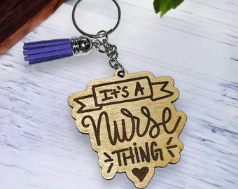 May include: Wooden keychain with a purple tassel. The keychain has the text "It's a Nurse Thing" with a small heart at the bottom.