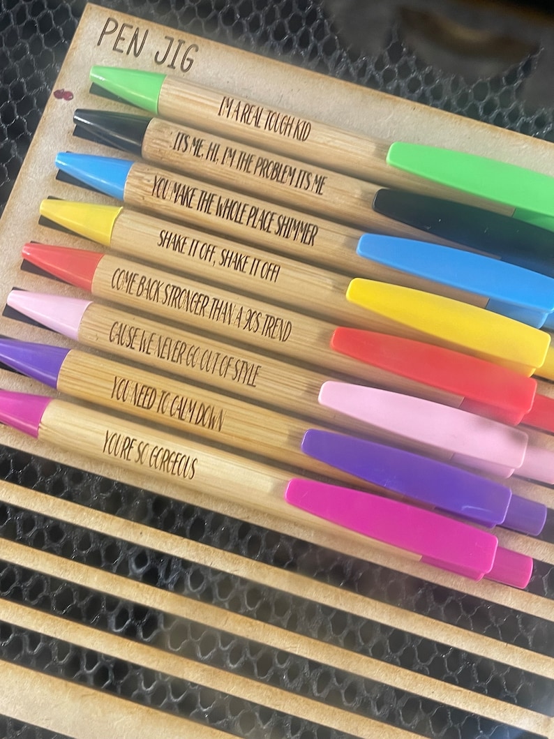 K&ouml;nnte beinhalten: Ein Set aus zehn Bambus-Stiften mit bunten Kappen und inspirierenden Zitaten, die in den Schaft graviert sind. Die Zitate beinhalten "Ich bin ein echter harter Kerl", "Du l&auml;sst den ganzen Ort gl&auml;nzen", "Komm st&auml;rker zur&uuml;ck als ein 90er-Jahre-Trend" und "Du bist so wundersch&ouml;n".