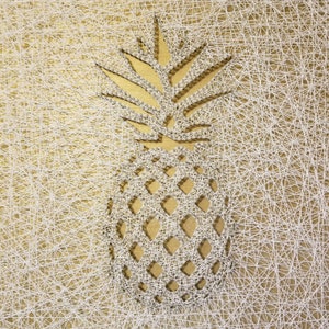 May include: A white string art pineapple design on a gold background. The pineapple is made of white string wrapped around nails hammered into the gold surface.