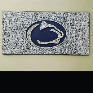 May include: A white string art design of a blue and white Nittany Lion logo on a wooden frame.