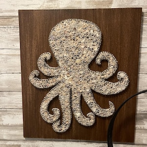 May include: A brown wooden framed wall art piece featuring a white string art octopus made with seashells.