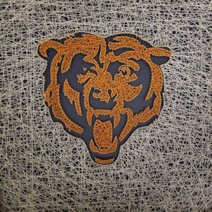 May include: String art of a bear's head with orange thread on a blue background.