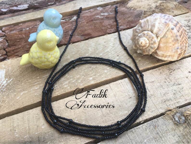 May include: A black beaded necklace with multiple strands. The necklace is made of small, round beads and is lying on a wooden surface.