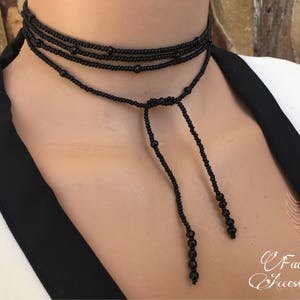 May include: A black beaded choker necklace with a long, adjustable tassel. The necklace is made of small, round beads and has a simple, elegant design.
