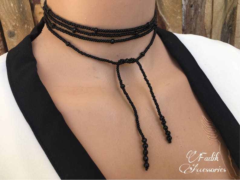 May include: A black beaded choker necklace with a long, adjustable tassel. The necklace is made of small, round beads and has a simple, elegant design.
