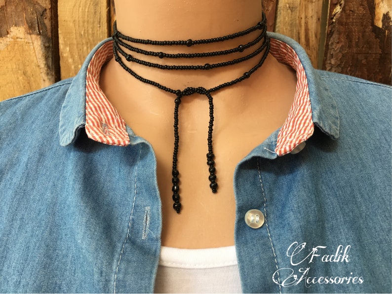 May include: A black beaded choker necklace with a long tassel. The necklace is layered with multiple strands of beads and has a simple, elegant design.