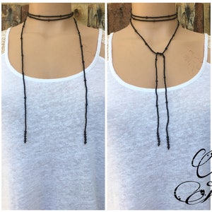 May include: A black beaded choker necklace with long, dangling strands. The necklace is shown on a model wearing a white vest top.