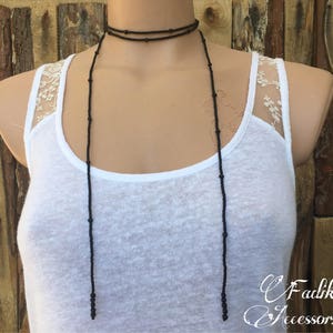 May include: A long black beaded necklace with two strands. The necklace is worn by a person wearing a white tank top with a lace overlay.