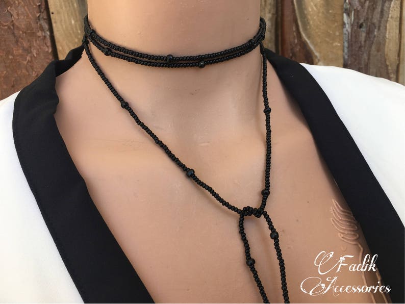 May include: A black beaded choker necklace with a long, dangling chain. The necklace is made of small, round beads and has a simple, elegant design.
