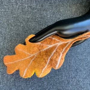 May include: A hand-felted oak leaf in shades of yellow, orange, and brown with white veins. The leaf is a decorative piece for home decor or a unique gift.