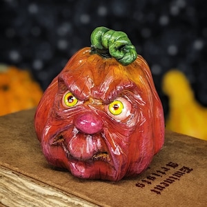 May include: A Halloween pumpkin sculpture with a menacing expression. The pumpkin is painted in red and orange hues, with a green stem and yellow eyes. It rests on a brown surface, perfect for spooky decor.