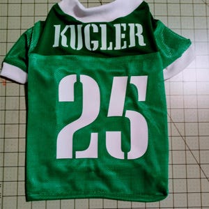 Pu&ograve; includere: Maglia da calcio per cani verde e bianca con il nome "KUGLER" e il numero "25" stampato sul retro.