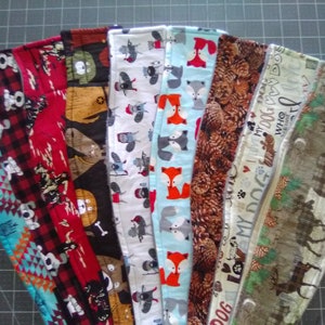 May include: A collection of fabric dog collars with various patterns. Designs include foxes, pinecones, dogs, and a turquoise geometric pattern. The collars are arranged in a fan shape, showcasing the variety of available styles and colors.