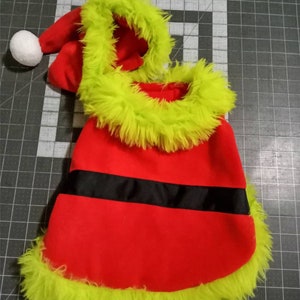 May include: Red and green dog costume with a white pom-pom on the hat. The costume has a black belt and a green fur trim.