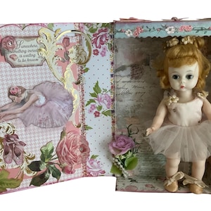 May include: A vintage doll in a pink tutu inside a decorative box. The box is adorned with floral patterns, a ballerina image, and the text "Somewhere incredible is waiting to be known."