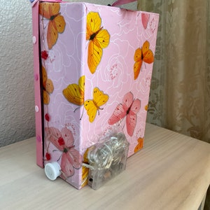 May include: A pink cardboard box with a butterfly pattern. The box has a white switch on the side and a clear plastic cord with lights coming out of the bottom.