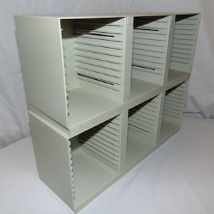 May include: A beige plastic storage unit with six compartments for organizing items. Each compartment has a series of slots for holding items.