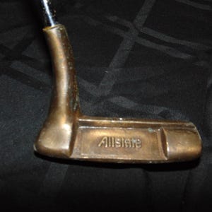 以下が含まれることがあります： ブロンズ色のヘッドと黒いシャフトが付いた、ヴィンテージのゴルフパター。「Allstate」の文字がパターヘッドに刻印されています。グリーン上での精度とコントロールのために設計されたパターです。