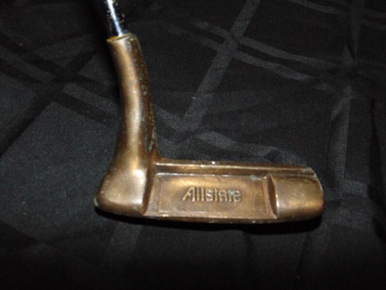 以下が含まれることがあります： ブロンズ色のヘッドと黒いシャフトが付いた、ヴィンテージのゴルフパター。「Allstate」の文字がパターヘッドに刻印されています。グリーン上での精度とコントロールのために設計されたパターです。