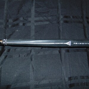 以下が含まれることがあります： 白いストライプと「GOLF PRIDE」の文字が入った黒いゴルフクラブグリップ。 グリップには白い三角形のロゴがあり、黒い背景にあります。 グリップは円筒形で、星のデザインがあります。