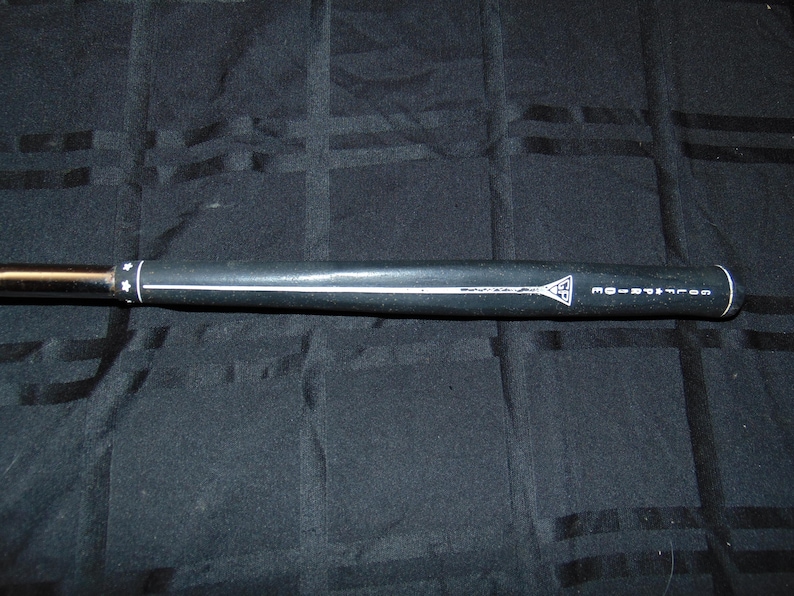 以下が含まれることがあります： 白いストライプと「GOLF PRIDE」の文字が入った黒いゴルフクラブグリップ。 グリップには白い三角形のロゴがあり、黒い背景にあります。 グリップは円筒形で、星のデザインがあります。