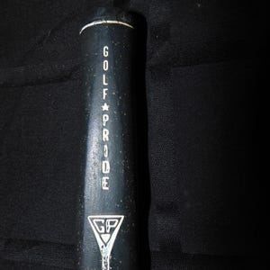 以下が含まれることがあります： 白い文字で「GOLF PRIDE」と書かれた黒いゴルフクラブグリップ。 グリップの上部には白いストライプがあり、三角形の中に「GP」が入った白いロゴが付いています。