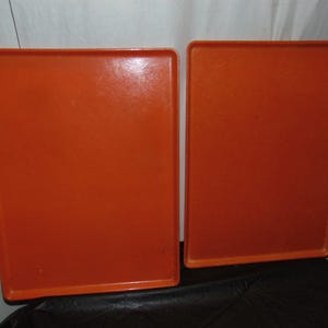 May include: Two rectangular orange trays with slightly raised edges. The trays are side by side, and the color is a solid, vibrant orange. The trays appear to be made of a smooth, possibly plastic material.