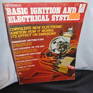 May include: A red and white book titled "Basic Ignition and Electrical Systems" with a picture of a car engine part on the cover. The book is a 3rd revised edition and costs $2.00. The book cover also includes the text "Chrysler's New Electronic Ignition: How It Works, Its Effect on Emissions".