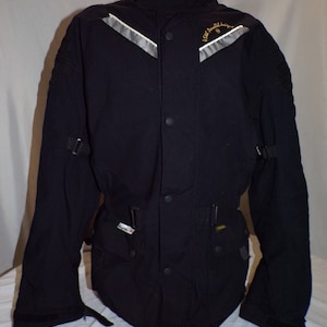 May include: Black motorcycle jacket with a high collar, snap closure, and reflective accents. The jacket has a logo that reads "Isle of Man TT" on the left shoulder.