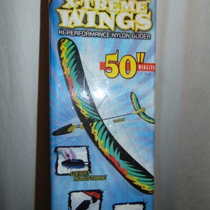 May include: A blue box with the text "X-Treme Wings" and "Hi-Performance Nylon Glider". The box features a colorful glider with a 50-inch wingspan. Additional text includes "Weight Adjustable" and "Designed for Durability".