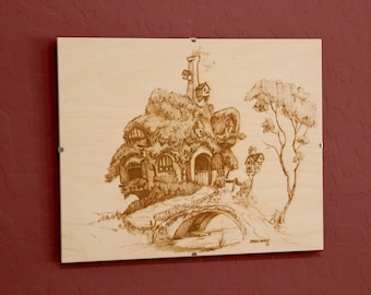 May include: A wood-burned image of a whimsical house with a bridge leading to it, surrounded by trees. The house is built into the side of a hill and has a chimney and several windows. The image is on a light brown wooden background.