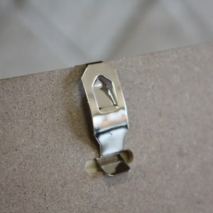 May include: A silver metal hanging hook attached to the back of a picture frame.